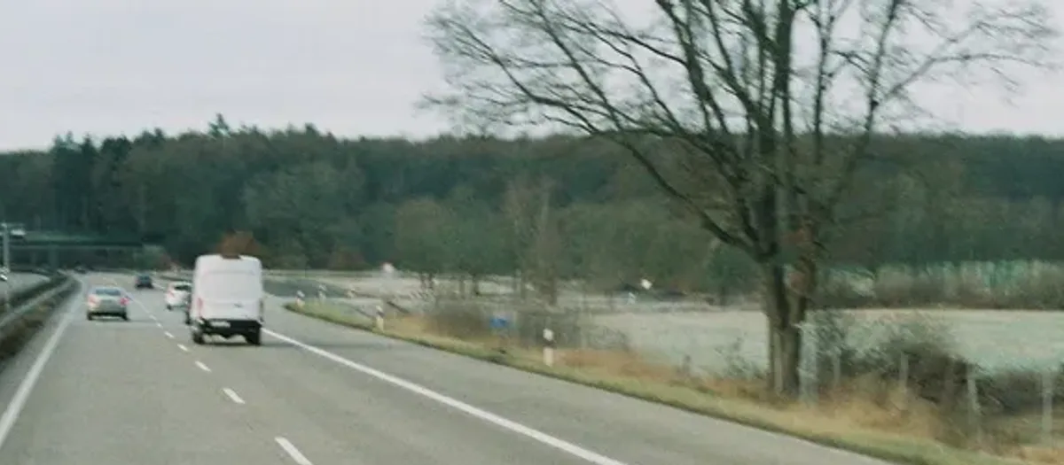 Weißer Kastenwagen fährt auf der rechten Spur einer Autobahn am Waldrand entlang
