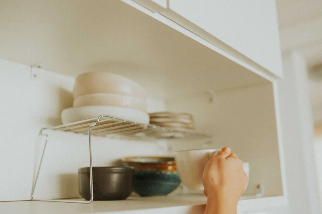 Offener Küchenschrank mit Tellern, Schüsseln und Töpfen, eine Hand räumt Geschirr heraus