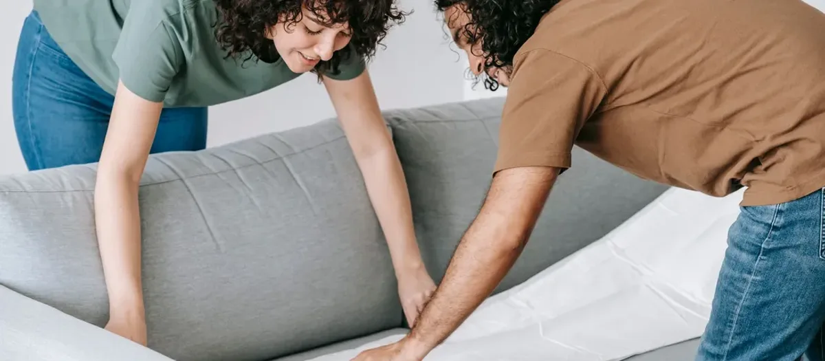 Zwei Personen heben ein graues Sofapolster gemeinsam auf das Couchgestell