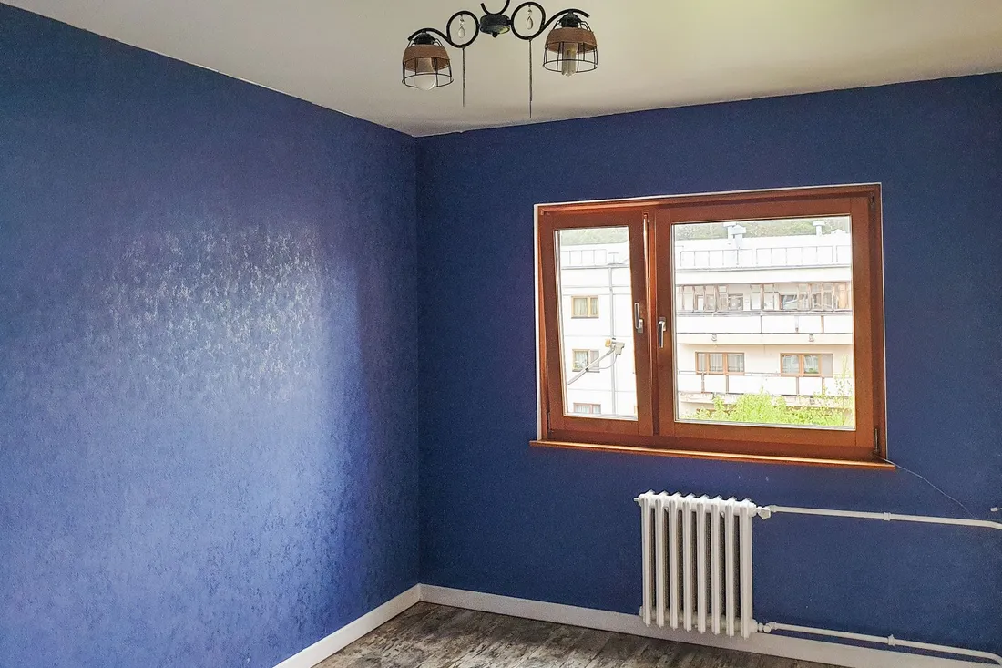 Leer geräumtes Zimmer mit dunkelblauen Wänden, Fenster und weißem Rippenheizkörper